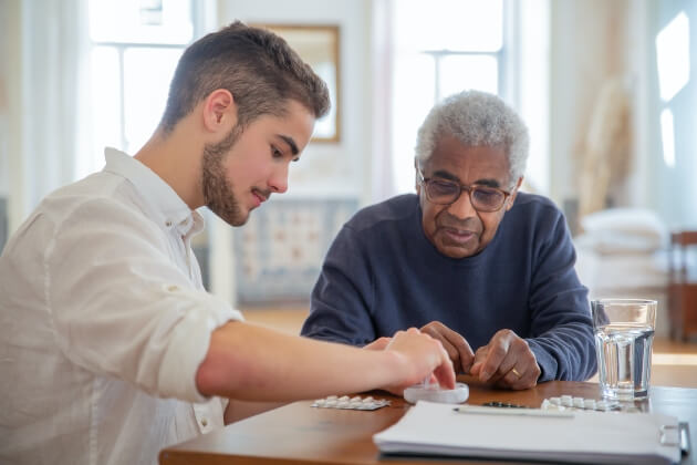 An older gentleman being assisted with his medications by a young man with a clipboard.